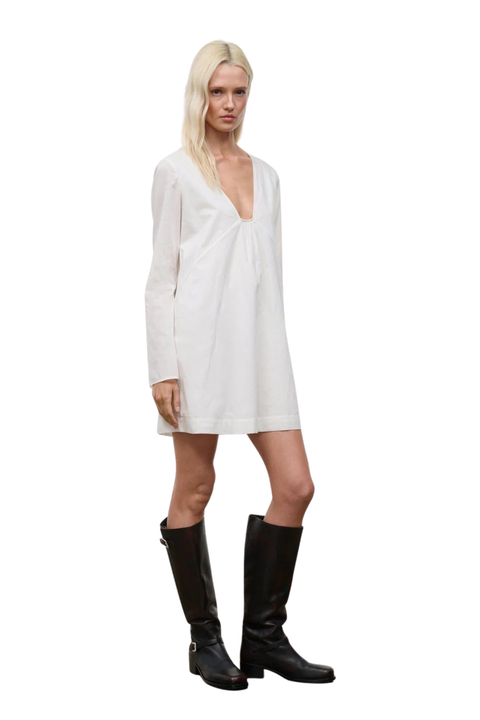 Side angle of a woman wearing a low cut, long sleeve white mini dress