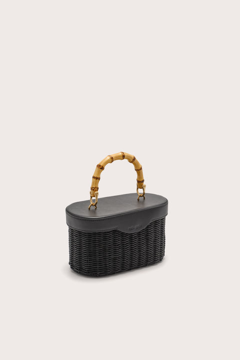 Side angle of a black woven handbag with bamboo handle on a light beige background