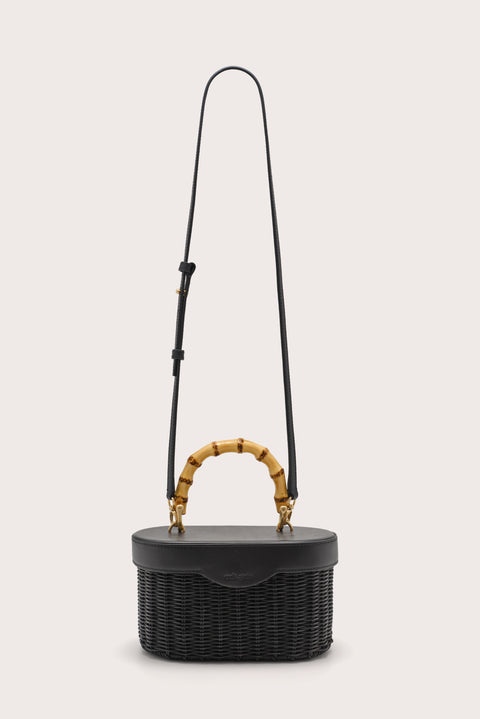 Black woven handbag with bamboo handle and a detachable black crossbody strap on a light beige background
