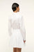 Back view of a woman wearing a long sleeve, white mini dress that features a collar and button down detail and a curved yoke at the hem. 