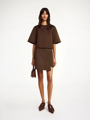 Woman wears brown satin short sleeve top with matching skirt.