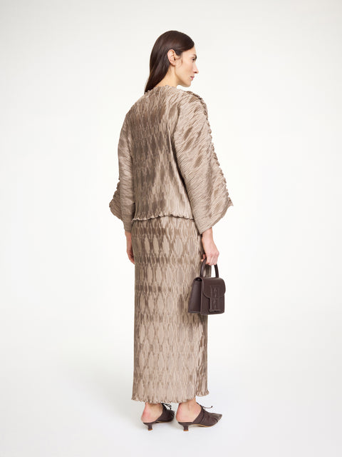 Back-facing woman wearing a textured beige top that features wide sleeves and a boatneck neckline, paired with a matching skirt.