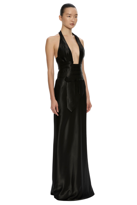 A model wearing a floor-length black satin halter gown with a deep plunging neckline and a matching wide waist sash, photographed against a solid white background.