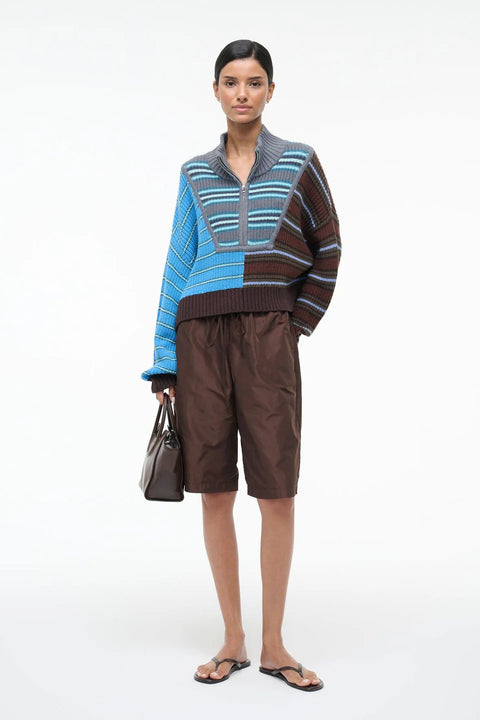 Woman wearing a patterned sweater and brown shorts on a white background
