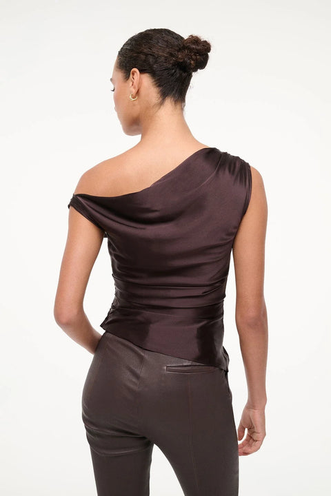 Back view of an asymmetrical, brown silk top that features an off-the-shoulder design and ruched draping throughout, paired with brown capris.