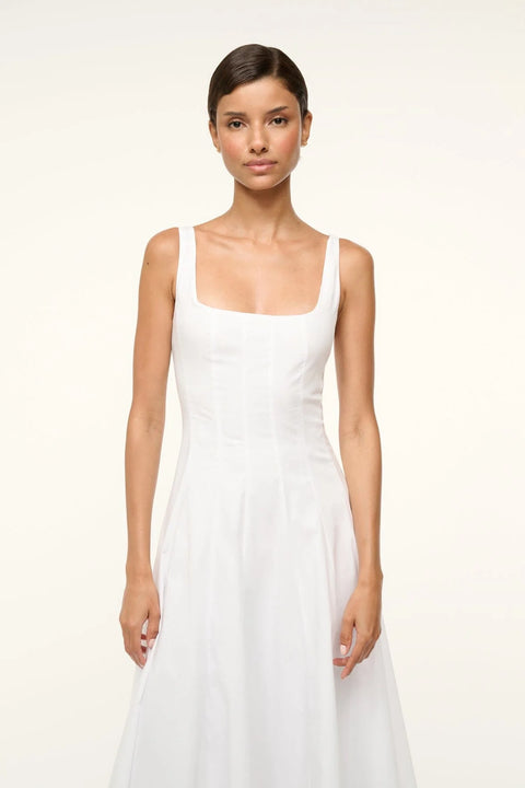Close up of a woman wearing a sleeveless white midi dress that features a square neck, corset-style paneling. 