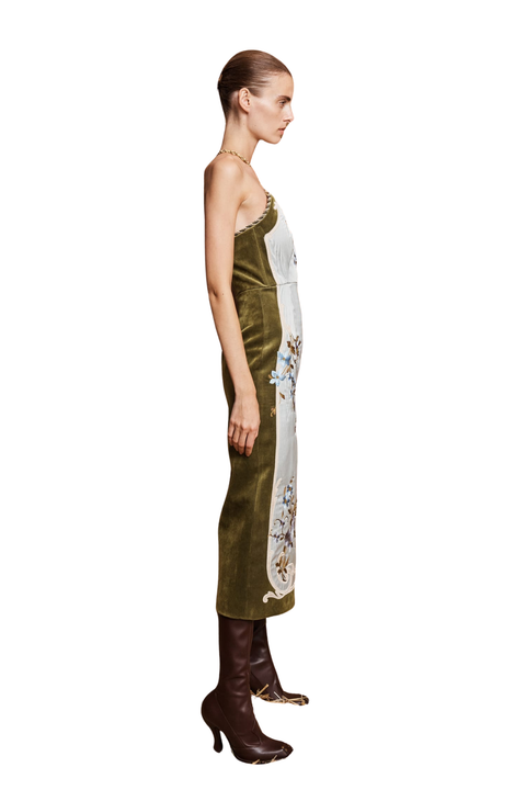 A model shown in profile wearing a strapless olive green velvet midi dress with a white vertical panel, floral embroidery, and brown knee-high boots against a plain white background.