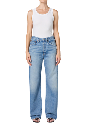 A model wearing a pair of light blue wide-leg denim jeans with a faded wash, styled with a white tank top and black sandals against a plain white background.