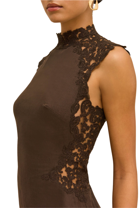 A close-up side view of a model wearing a sleeveless high-neck dress in dark brown with intricate floral lace applique along the shoulder and side.