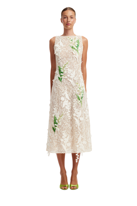 A model wearing a sleeveless cream lace midi dress with green floral applique, paired with lime green high-heeled sandals, against a plain white background.