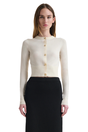 Woman wearing a cream-colored cardigan with gold buttons on a white background