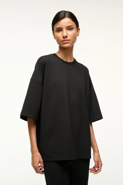 Close up of a woman wearing a black oversized knit t-shirt with matching cropped pants. 