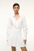 Close up of a woman wearing a long sleeve, white mini dress that features a collar and button down detail and a curved yoke at the hem. 