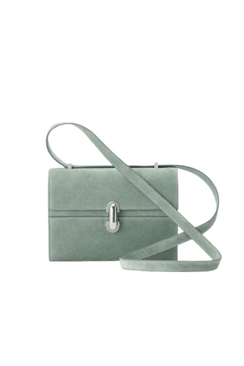 A mist green suede crossbody handbag that features a silver hardware twist lock and a crossbody strap. 