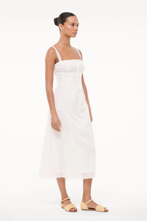 Side-facing woman wearing a white midi dress and nude sandals. 