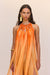 Close up of the top of a woman wearing a bright orange maxi dress that features intricate woven cutouts with gold bead accents on the high neck line, with panels of silk cascading from the chest.