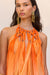 Detail shot of the woven, high neck line of an orange maxi dress that shows ribbons of silk woven together with gold beads before cascading down the rest of the dress. 