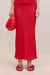 Close up of a woman wearing a bright red silk maxi skirt in a flattering bias cut, styles with a red top and red accessories. 