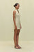Side angle of a woman wearing a khaki high-neck mini dress that features a utility design, front zipper, and sleek side pockets, paired with black sandals.  