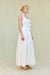 Side view of a woman wearing a white cropped halter top that features a square neckline with an adjustable tie-front bow, paired with a white maxi skirt. 