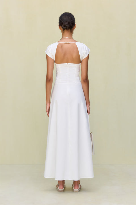 Back view of a woman wearing a white maxi poplin dress that features an open back and cap sleeves. 