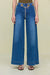 Up close of a woman wearing blue low-rise, wide leg jeans that feature gold metal grommets along the waist and a Cult Gaia logo chain belt, paired with a green bodysuit. 