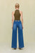 Back view of a woman wearing an olive green sleeveless bodysuit that features a mock neck, paired with blue wide leg jeans. 
