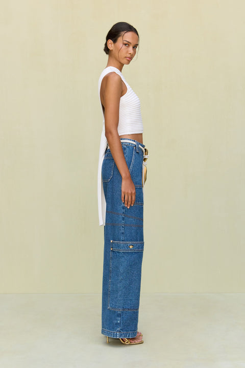 Side view of a woman wearing a white, one shoulder knit crop top that features a tie in the back. 