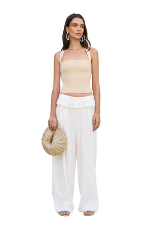 Woman wearing a beige top and white pants holding a straw bag on a white background