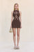 Woman wearing a brown sleeveless mini dress that features floral cutouts across the body, paired with a tan handbag and tan sandals. 