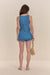 Back view of a woman wearing a blue denim mini skort that features a front to back wrap detail that exposes the hem of the shorts in the back, paired with a matching denim top. 