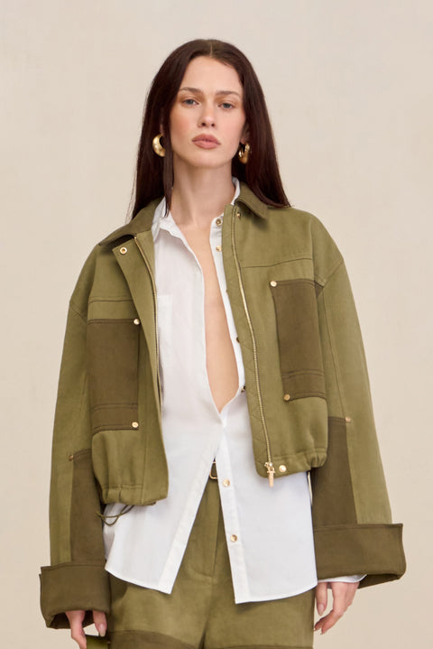Woman wearing a two-tone green cropped barn-style jacket over a white button down and matching pants. 