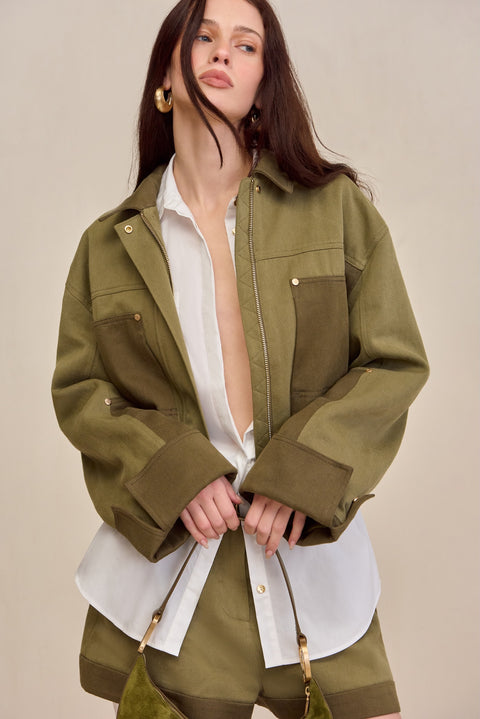 Woman wearing a two-tone green cropped barn-style jacket over a white button down and matching pants. 
