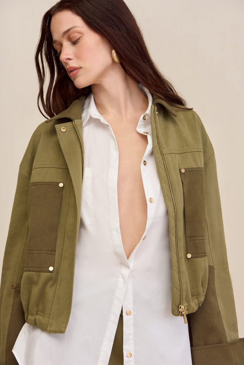 Close up of a woman wearing a two-tone green cropped barn-style jacket over a white button down and matching pants. 