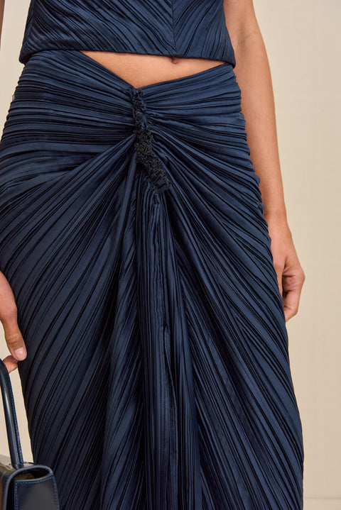 Detail shot of a navy midi skirt that features an asymmetrical, slight V waistline with knotted ruching at the hip. 