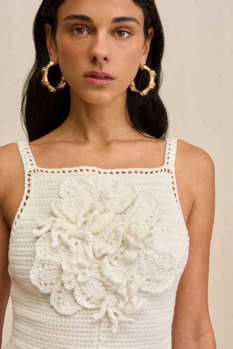 Close up of a woman wearing a white crochet romper with floral details against a beige background