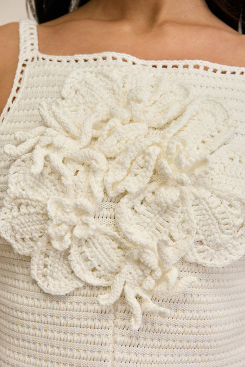 Close up of a woman wearing a white crochet romper with floral details against a beige background