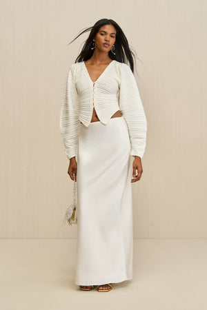 Woman wearing a white structured cardigan paired with a white maxi skirt. 