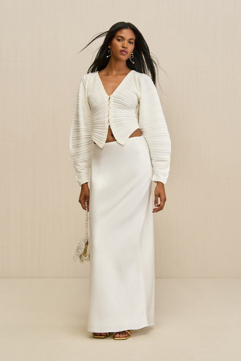 Woman wearing a white structured cardigan paired with a white maxi skirt. 