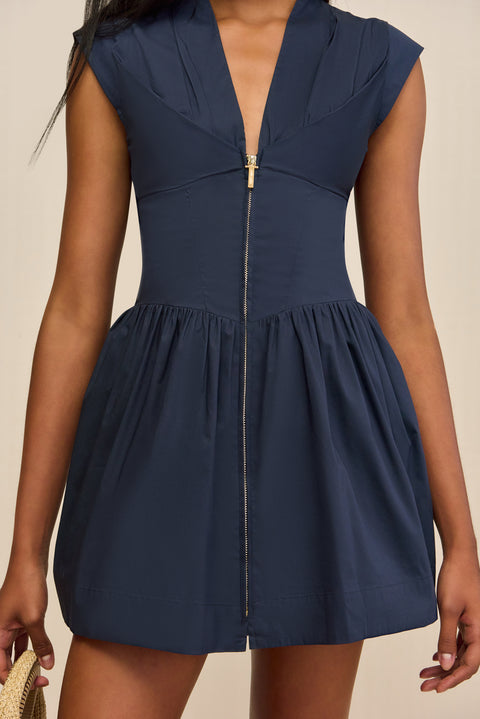 Detail shot of a woman wearing a navy poplin mini dress that features a deep V, fitted bodice, and structured skirt, with a gold-toned front-sipper closure. 