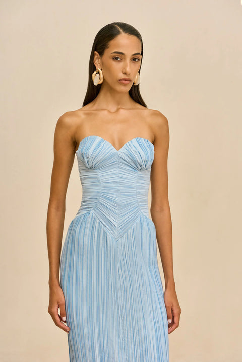 Detail shot of woman wearing a light blue strapless pleated dress against a beige background.