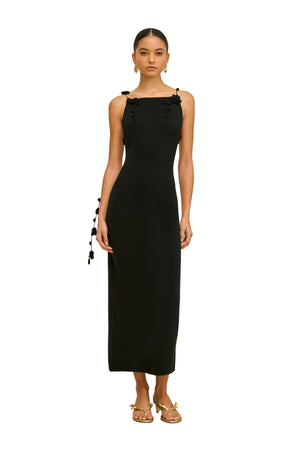 Woman wearing a black sleeveless dress with hanging floral straps on a beige background
