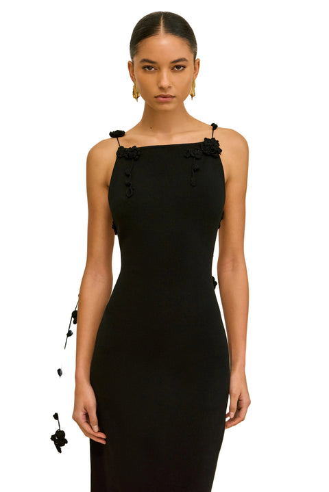 Close up shot of woman wearing a black sleeveless dress with hanging floral straps on a beige background