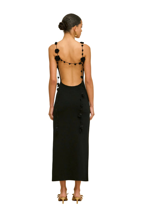 Back-facing woman wearing a black sleeveless dress with hanging floral straps on a beige background