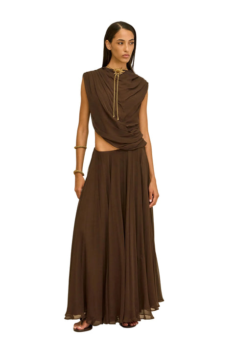 Woman wearing a brown outfit with a draped top and long skirt on a beige background