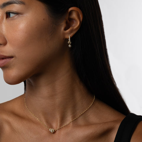 Woman wearing an 18k yellow gold mini hoop earring that is pave with white diamonds and features three 18k gold annulets, one with a dangling white diamond charm. 