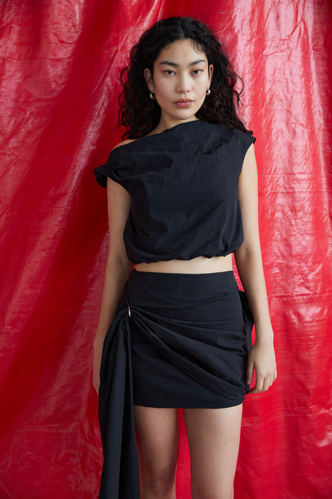 Model in front of a red background wearing the black cloud skirt with draping.