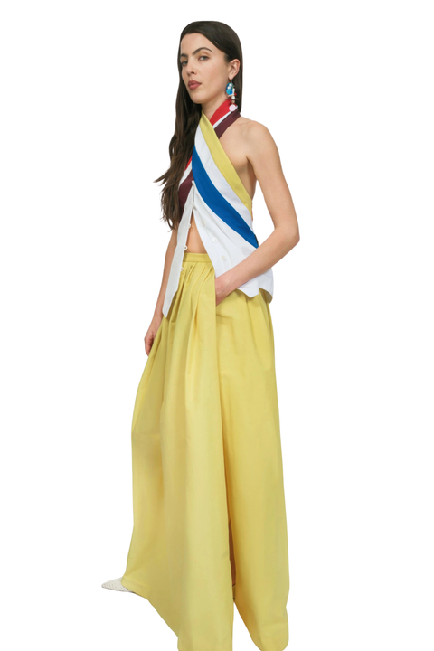 A woman wearing a white top with rainbow halter neck ties and a matching yellow skirt