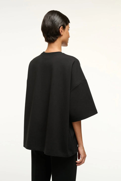 Back view of a woman wearing a black oversized knit t-shirt with matching cropped pants. 