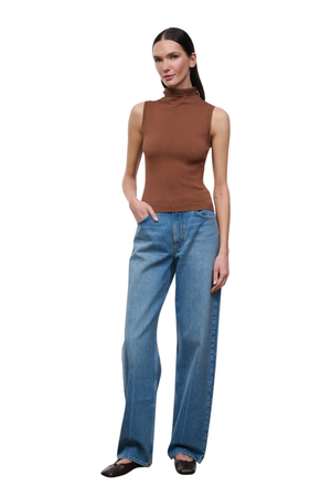 A woman modeling a sleeveless brown mock-neck top and wide-leg blue jeans against a plain white background.